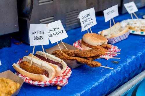 A variety of food items on a blue table, including hot dogs, chicken schnitzel sandwiches, and chicken-on-a-stick.