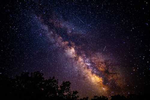 A stunning view of the Milky Way galaxy filled with stars and a few shooting stars against a dark night sky.