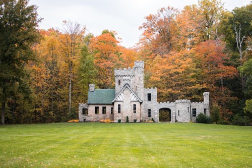 A stone castle surrounded by vibrant autumn trees and a green lawn.