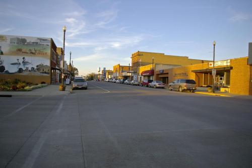 A quiet downtown street lined with brick buildings and parked cars under a clear blue sky.
