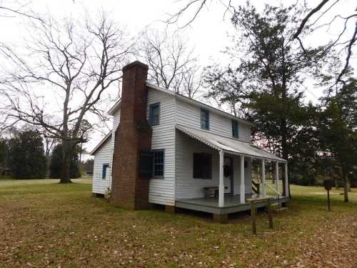 A white two-story house with a porch and chimney, surrounded by trees and grass in a rural setting.