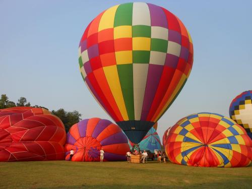 Colorful hot air balloons on a grassy field, with people preparing them for flight under a clear blue sky.