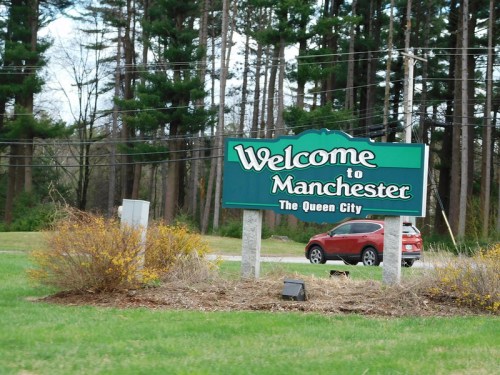 Welcome sign for Manchester, labeled "The Queen City," surrounded by greenery and trees.