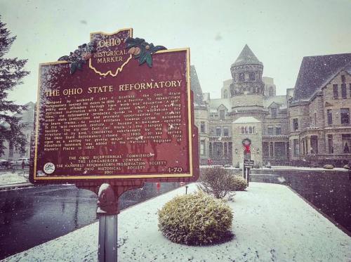A historical marker in front of the Ohio State Reformatory, surrounded by snow and a historic building in the background.