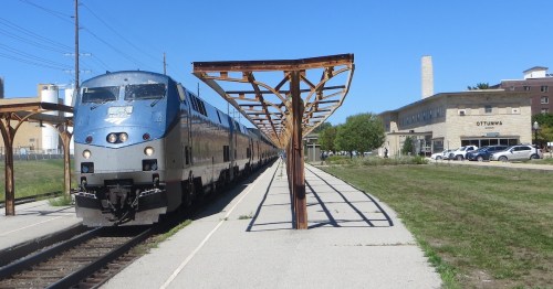 Amtrak train arriving at a station with a modern building in the background and clear blue skies.