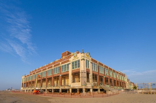 A large, historic building with a sandy beach in the foreground and a clear blue sky above.
