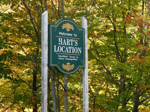 Welcome sign for Hart's Location, the smallest town in New Hampshire, surrounded by colorful autumn foliage.