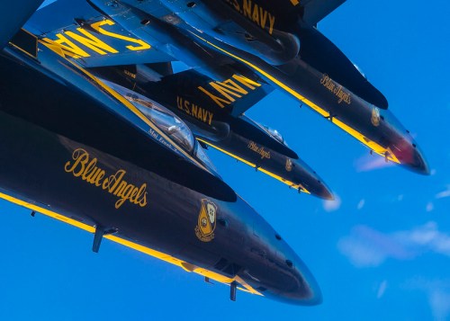 Three Blue Angels jets flying in formation against a clear blue sky.