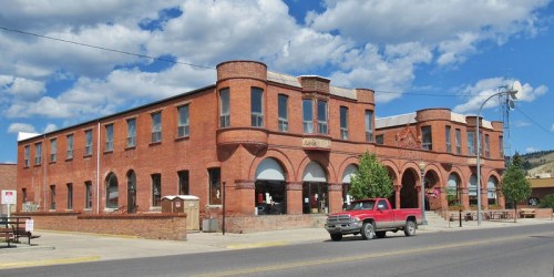 Historic red brick building with arched windows, surrounded by trees and a blue sky with clouds. A red truck is parked nearby.