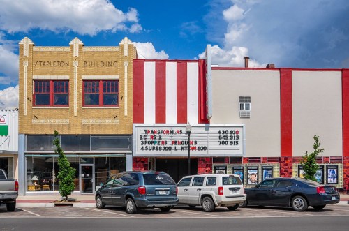 Historic theater building with a marquee displaying movie times, surrounded by parked cars and a blue sky.