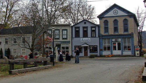 A quaint town street featuring historic buildings, a group of people, and autumn decorations.