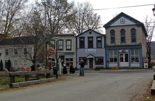 Historic buildings line a street with people gathered outside, surrounded by autumn trees and seasonal decorations.