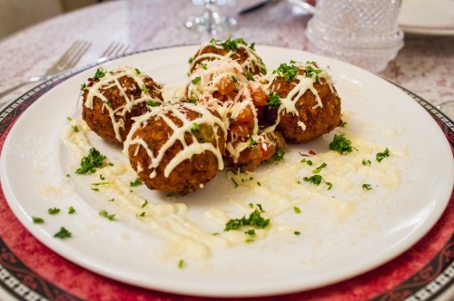 A plate of crispy fried balls topped with sauce, diced tomatoes, and herbs, served on a decorative table setting.