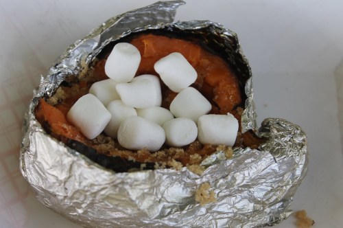 A baked sweet potato wrapped in foil, topped with mini marshmallows.