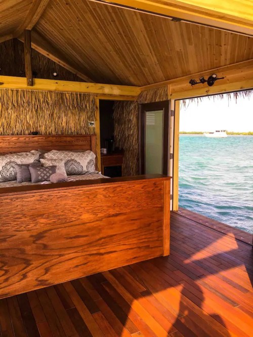 Cozy interior of a wooden hut with a bed, overlooking a serene water view. Natural materials and warm lighting.