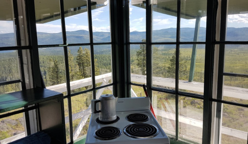 A stove in a glass-walled cabin with a stunning view of mountains and trees outside.
