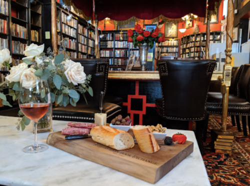 A cozy library setting with a charcuterie board, wine glass, and a floral arrangement on a marble table.