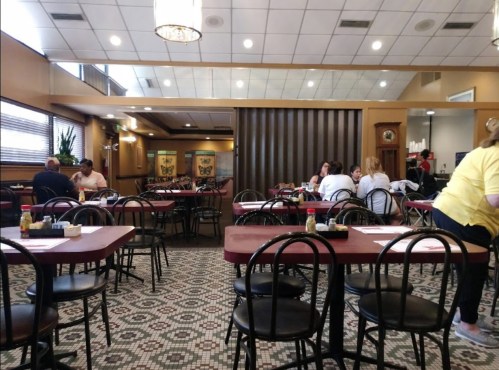 A spacious restaurant interior with empty tables, patrons dining, and a warm, inviting atmosphere.
