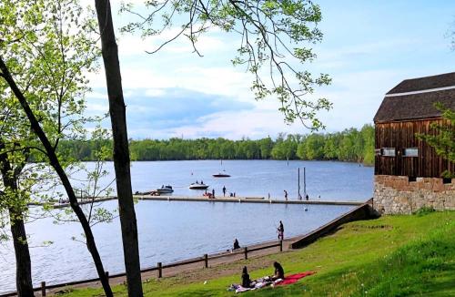 A serene lakeside scene with boats on the water, a wooden building, and people enjoying the grassy shore.