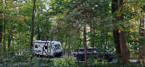 A camper and truck parked among lush green trees in a wooded area.