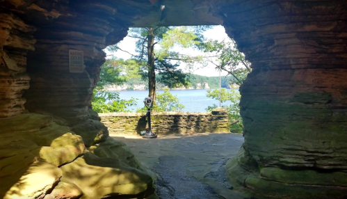 A scenic view through a rock formation, overlooking a lake surrounded by trees.