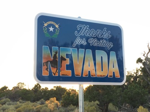 Sign welcoming visitors to Nevada, featuring the state emblem and a silhouette of a cowboy on horseback.