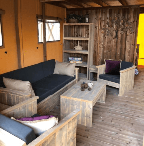 Cozy wooden lounge area with a sofa, chairs, and a coffee table, set in a rustic interior with warm lighting.