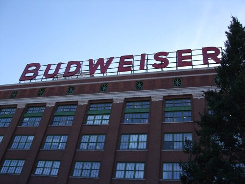 Signage of Budweiser on a brick building with green windows against a clear blue sky.