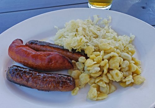 A plate with two grilled sausages, sauerkraut, and small pasta pieces, accompanied by a glass of beer.