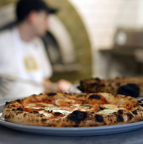 A close-up of a freshly baked pizza with melted cheese and toppings, with a blurred figure in the background.