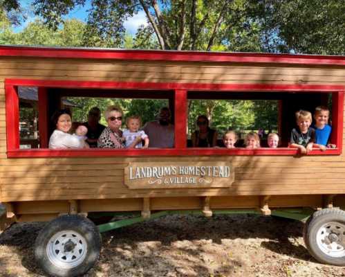 A group of people, including children and adults, smiling and posing in a wooden wagon at Landrum's Homestead.