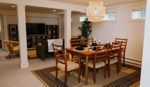 A cozy dining area with a wooden table, chairs, and a stylish light fixture, set in a well-lit room.