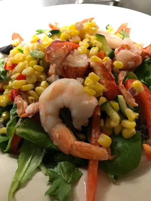 A colorful salad topped with shrimp, lobster, corn, and diced vegetables on a bed of mixed greens.