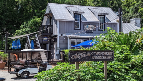 A rustic building with a metal roof, featuring a sign for "Old Town Dispensary" and outdoor seating under blue umbrellas.
