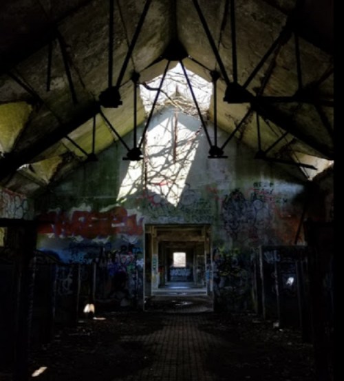 An abandoned building interior with graffiti on the walls and light streaming through a broken roof.