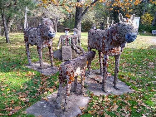 Sculptures of three animals made from stones and leaves, set in a grassy area surrounded by trees.