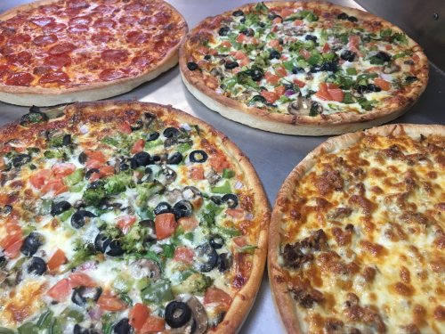 Four pizzas on a metal surface: pepperoni, veggie with olives and broccoli, and two cheese varieties.