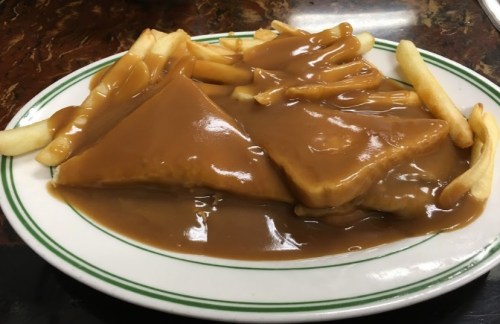 A plate of fries topped with two triangular pieces of bread smothered in brown gravy.