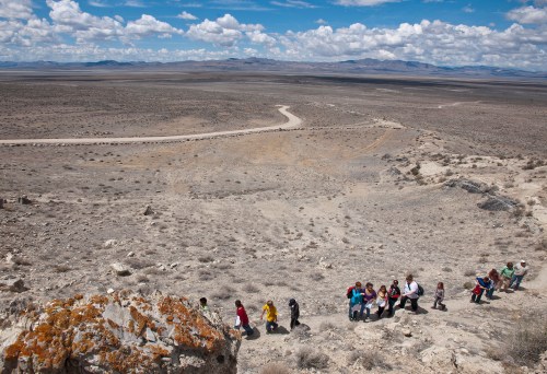 A group of people hiking down a rocky slope in a vast, arid landscape under a cloudy sky.