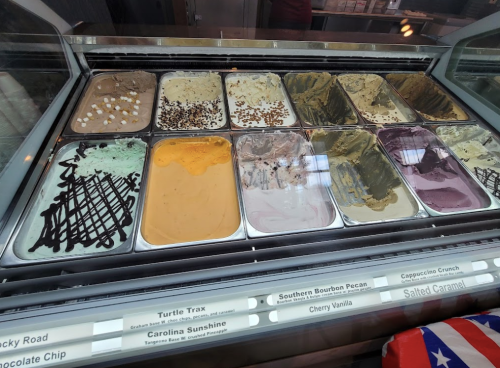 A display of various ice cream flavors in metal tubs, including mint, chocolate, and caramel options.