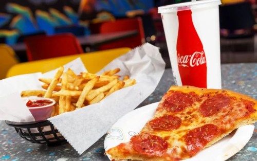 A slice of pepperoni pizza on a plate, with a side of fries and a Coca-Cola drink in a cup.
