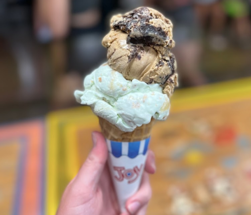 A hand holding a cone with three scoops of ice cream: chocolate, mint, and a cookie-flavored scoop on top.