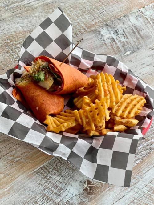 A red tortilla wrap filled with vegetables, served with a side of crispy waffle fries in a checkered basket.