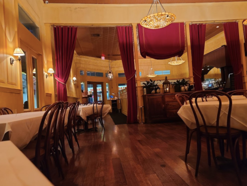 Cozy restaurant interior with wooden floors, yellow walls, and red curtains, featuring empty tables and warm lighting.