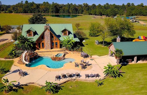 Aerial view of a spacious home with a pool, surrounded by greenery and a large lawn.