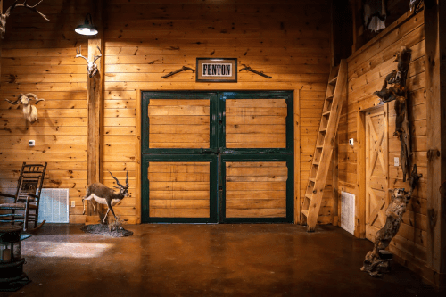Interior of a rustic wooden room featuring a green double door, mounted deer, and wooden decor.