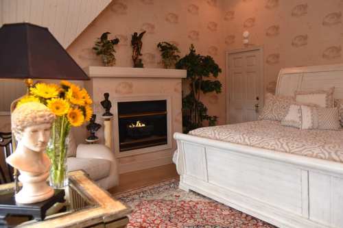 Cozy bedroom featuring a fireplace, decorative plants, a vintage lamp, and a floral arrangement on a table.