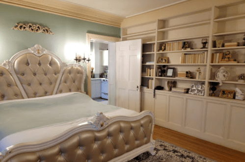 Elegant bedroom featuring a plush bed, decorative wall, and a bookshelf filled with books and decor.