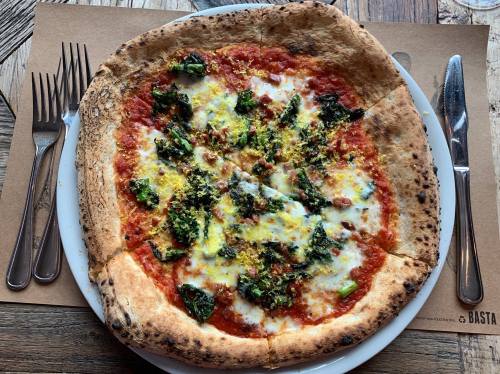 A freshly baked pizza topped with tomato sauce, mozzarella, and green vegetables on a wooden table.