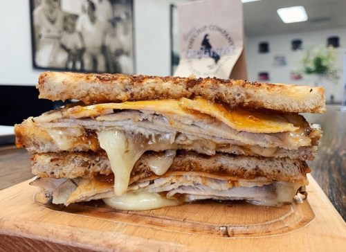 A stacked grilled cheese sandwich with melted cheese and layers of turkey on toasted bread, served on a wooden board.